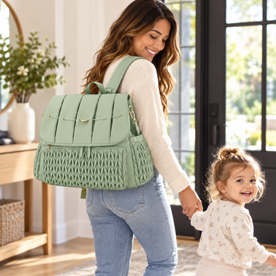 American mother and toddler in a bright entryway with the sage green quilted diaper bag worn as a backpack