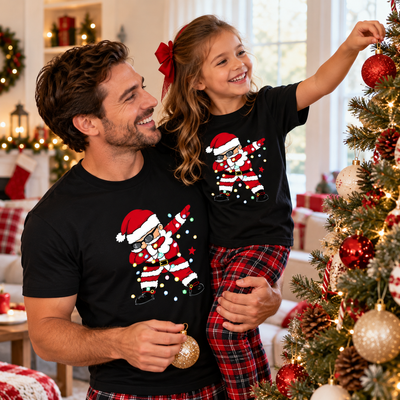 Dad and daughter in matching black dabbing Santa Christmas T-shirts hanging ornaments on the tree